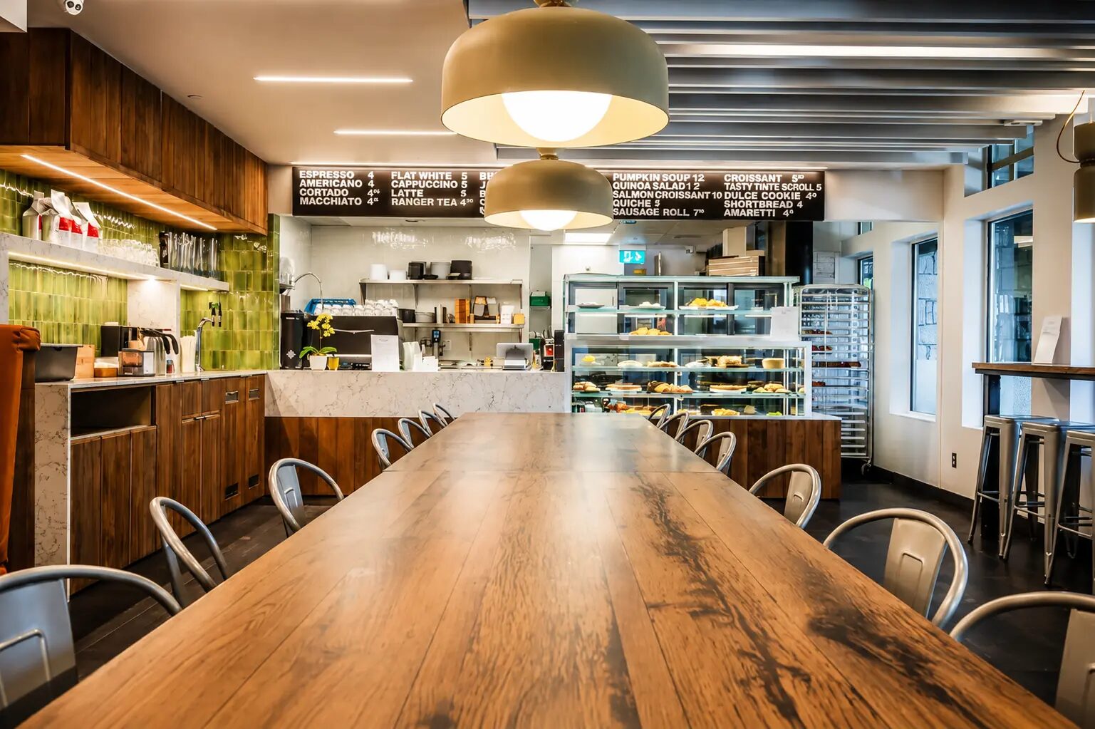 Alpha Café at Pinnacle Hotel Whistler Village with a long communal wood table, green-tiled espresso bar and fresh pastry case
